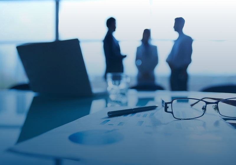 Business meeting silhouettes with office documents and glasses in foreground.