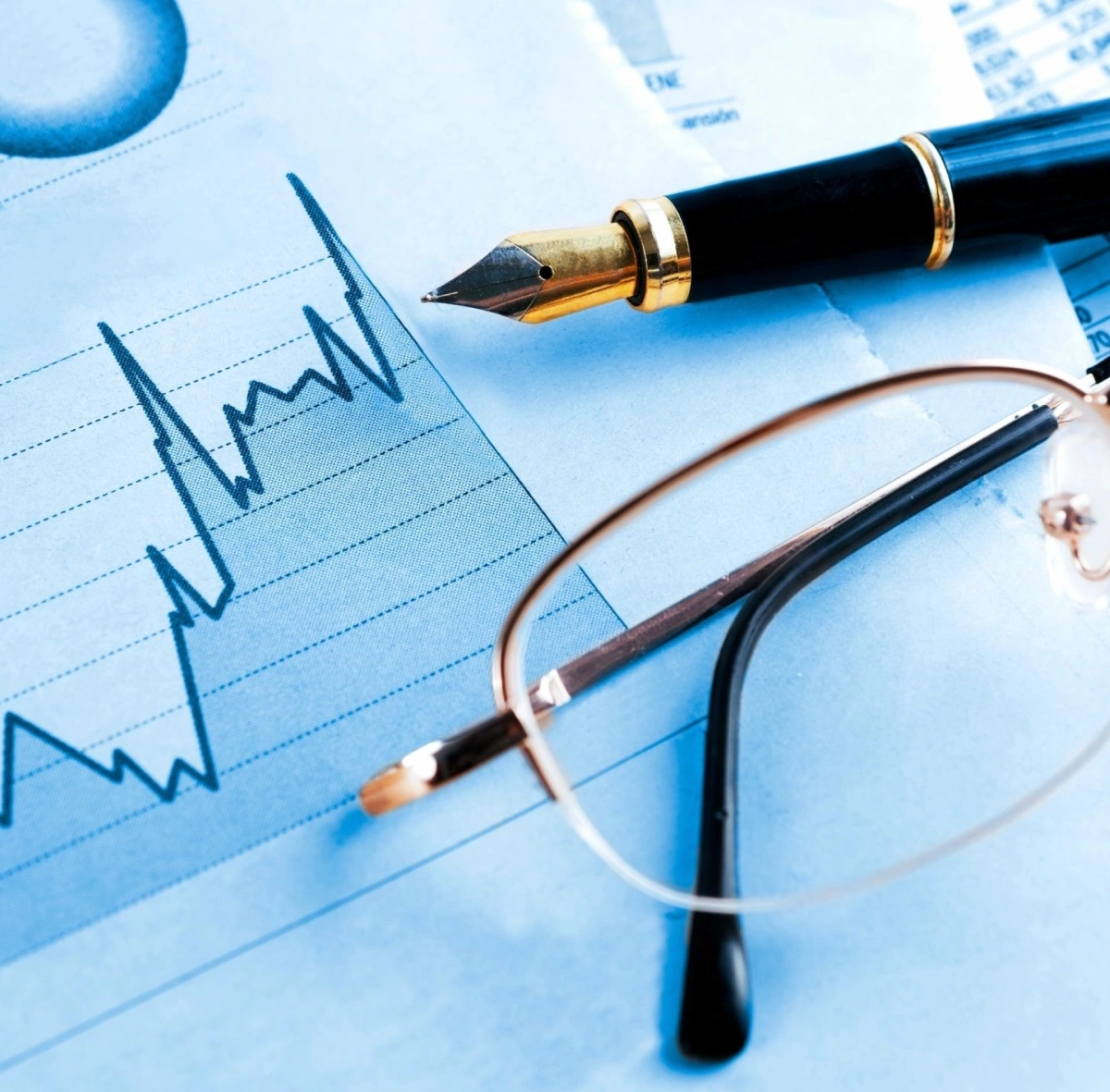 A pen and glasses resting on a financial chart with fluctuating data.