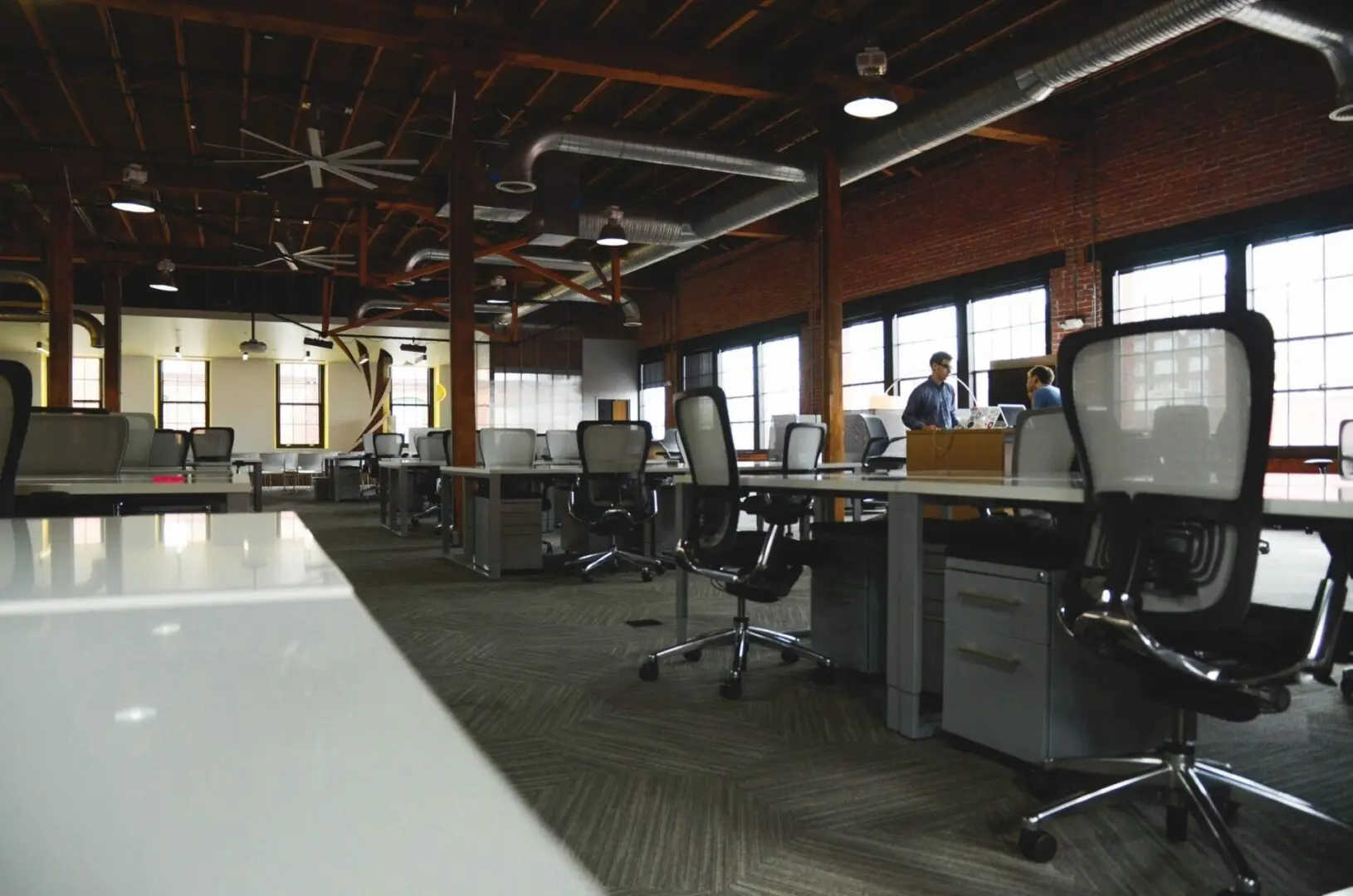Modern, open-plan office with desks and computers under industrial lighting.