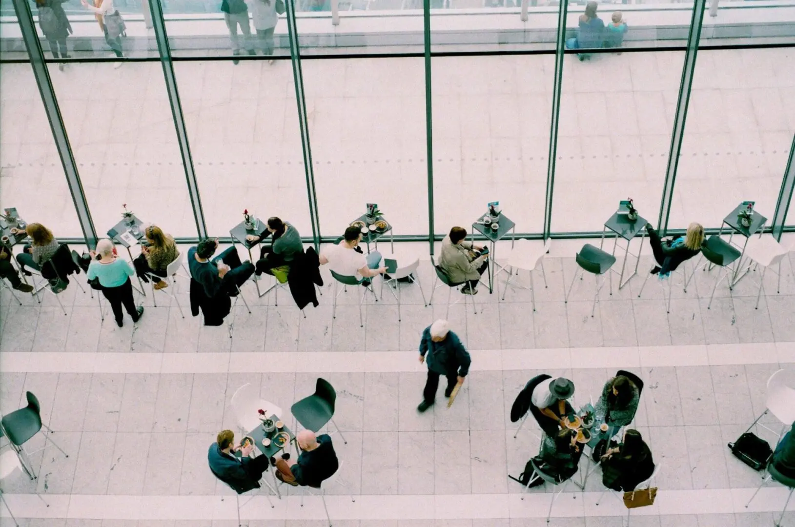 People walking and sitting in a modern glass-walled building lobby.