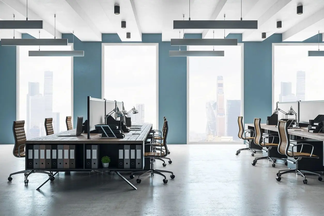 Modern office space with desks and computers near large windows.