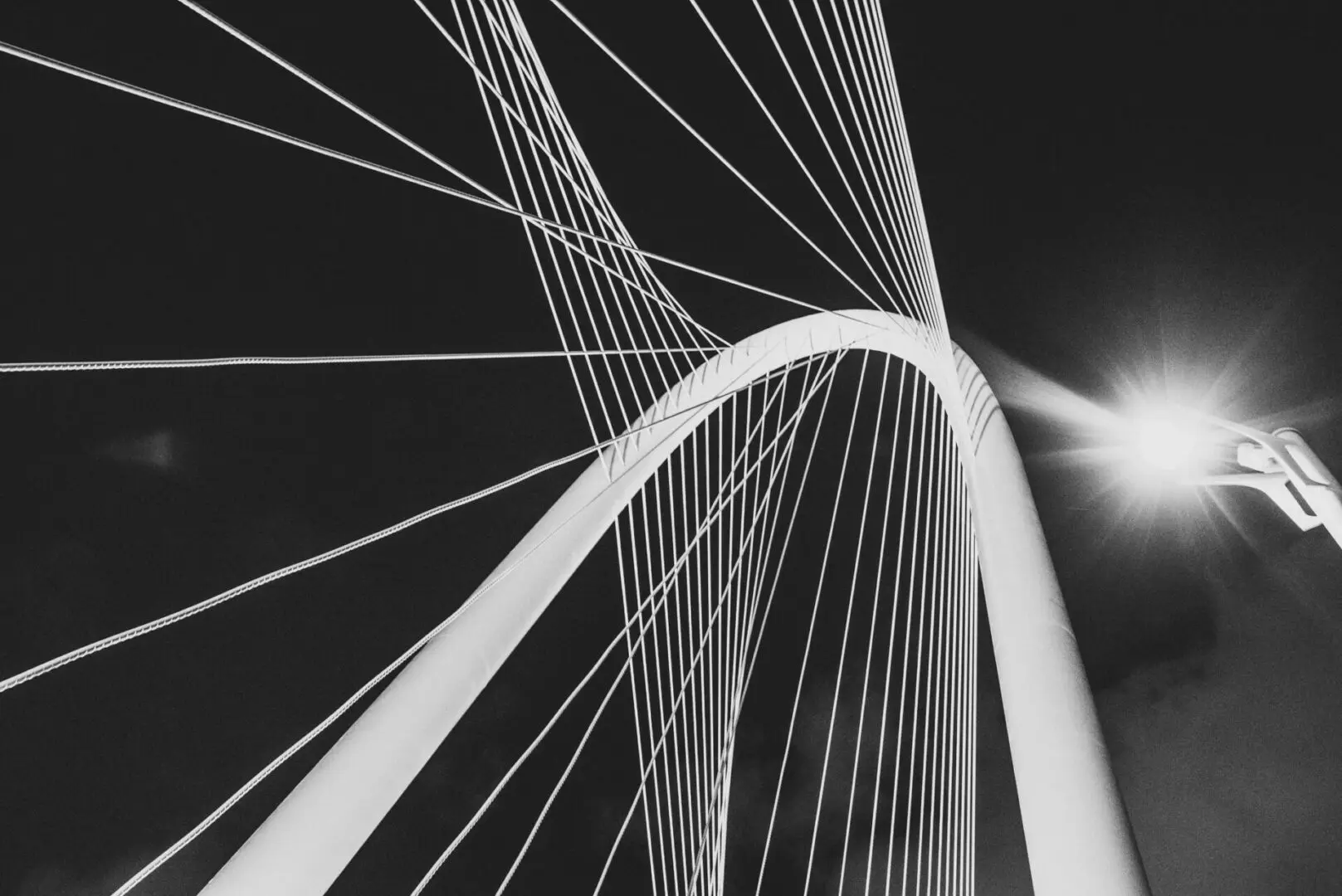 Abstract black and white image of a modern suspension bridge's cables and arch.